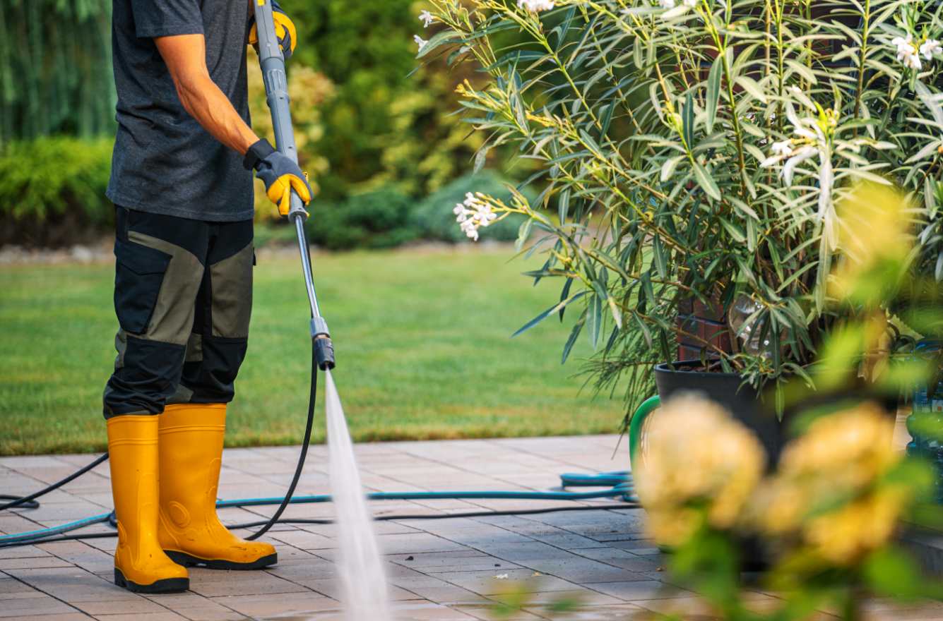 Professional patio cleaning service using pressure washer in garden on sunny day