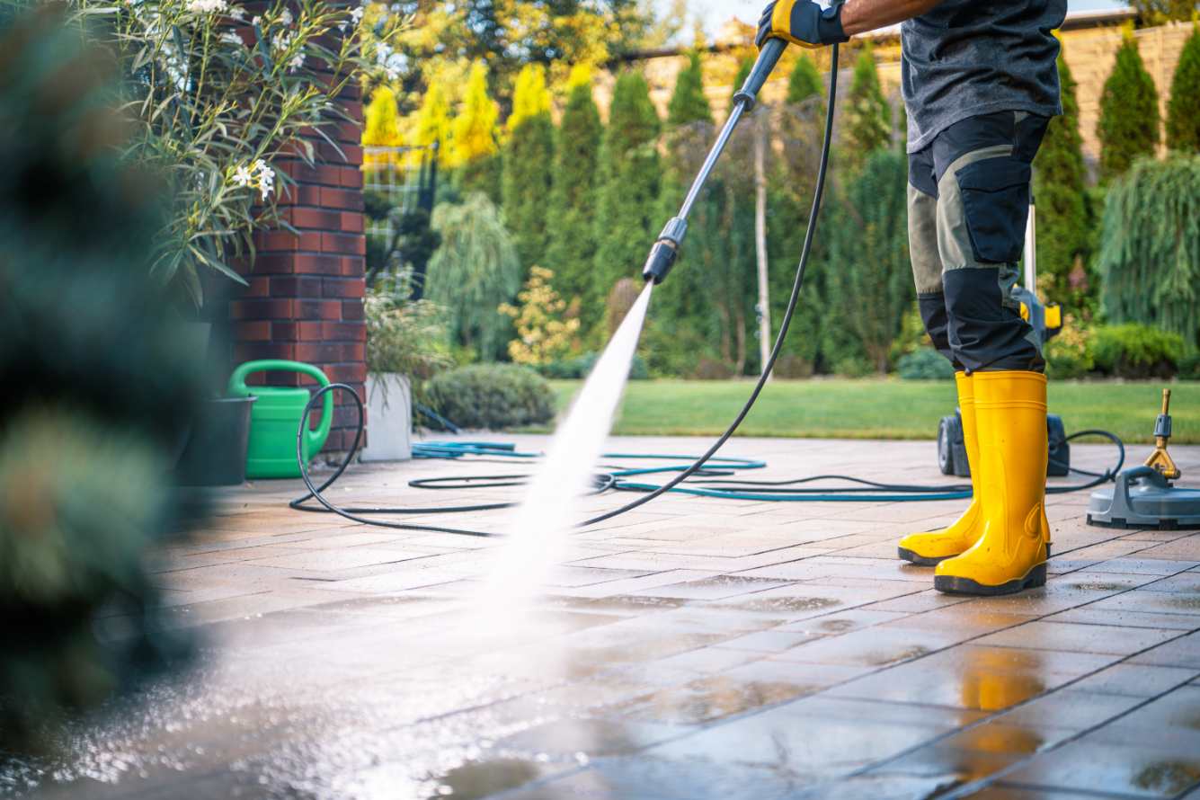 Professional pressure washing technician in yellow boots cleaning Boca Raton luxury property surrounded by golf course landscaping